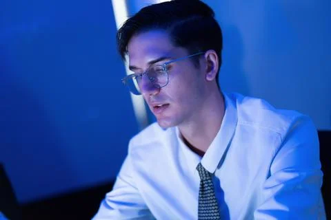 Young man working intently on a computer in a blue-lit environment during e.. Stock Photos