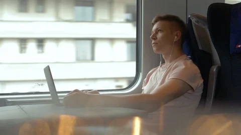 A young man is working on a laptop and listening to music in moving modern train Stock Footage 112435606