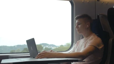 A young man is working on a laptop and listening to music in moving modern train Stock Footage 112436621