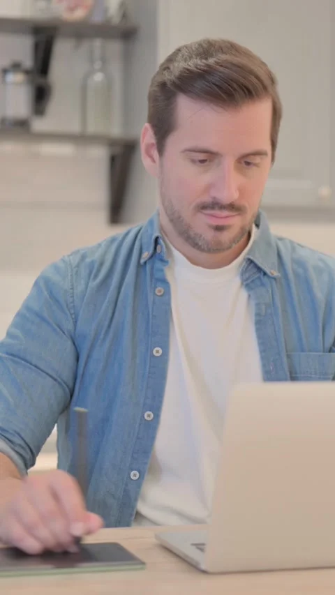 Young Man Working on Laptop and Graphic Tablet,  Designing, vertical video Vidéo 328565925
