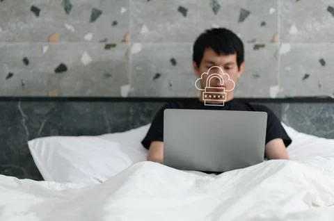 Young Man Working on Laptop with Cloud Security Concept in Bedroom 库存照片