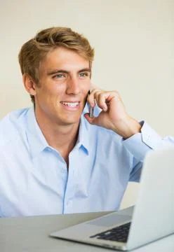 Young man working on laptop computer talking on phone Stock Photos