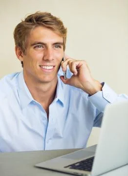 Young man working on laptop computer talking on phone Stock Photos