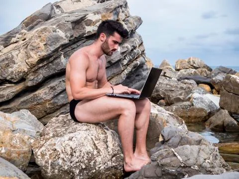 Young man working on laptop computer at beach Stock Photos