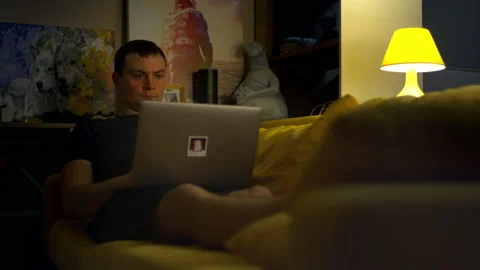 Young man working on a laptop on the couch at home. 4K, slow motion. Video stock 148393551