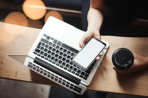 Young man is working on laptop, drinking coffee and holding cell phone. Stock Photos
