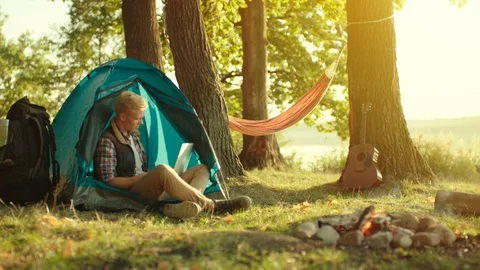 Young man working at laptop during camping with tents at sunset Stock Footage 98672047