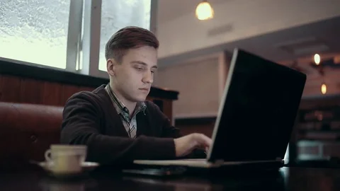 Young man working on a laptop while sitting in a cafe with a dark interior. Stock Footage 71565419