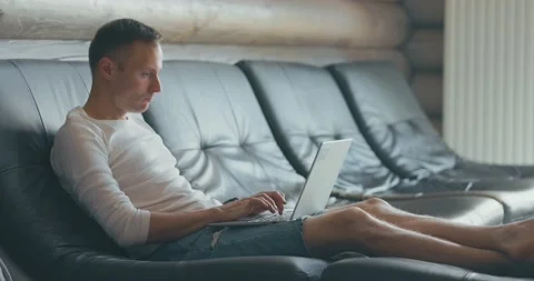 Young man is working on laptop while sitting on sofa in room Stock Footage 199511331