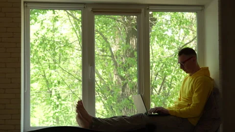 Young man working on laptop while sitting on windowsill Stock-Footage 308694033