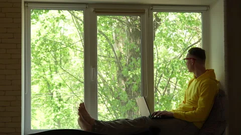 Young man working on laptop while sitting on windowsill Stock Footage 312010480