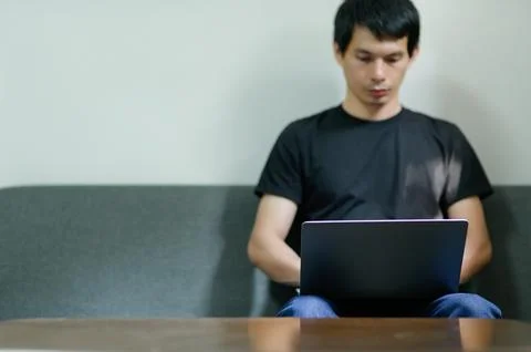 Young Man Working on Laptop While Sitting on Couch in Modern Room Stock Photos