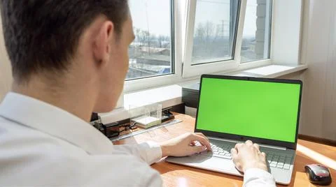 A young man working in an office using a laptop computer with a green screen on Stock-Fotos