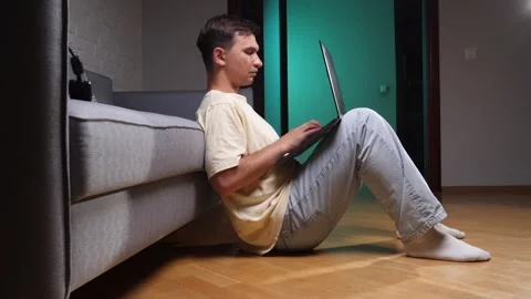 Young man working or studying remotely, sitting casually on floor leaning Stock Footage 342774108