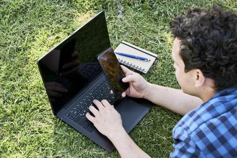 Young man working or studying using an smartphone and a laptop outdoors Foto stock