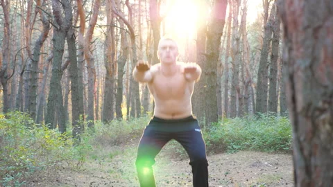 Young man working out in beautiful sunny forest. Sporty guy doing squats Vídeos de archivo 252367057