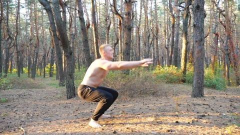 Young man working out in beautiful sunny forest. Sporty guy doing squats at Stock Footage 333982539
