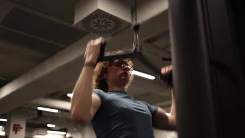 A young man is working out at the gym on machines, dreaming of achieving a sculp Stock Footage 301677261