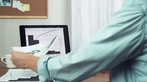 Young man working with printed analyzing graphs using digital tablet and laptop Stock Footage 81879617