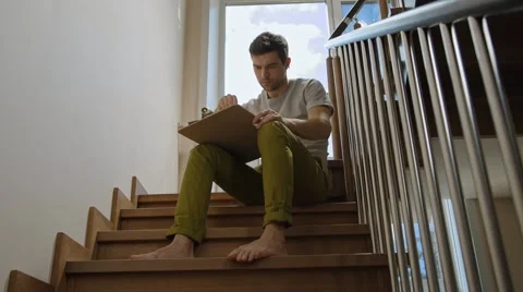 Young man working on a project sitting on the stairs in the cottage Stock Footage 45429959