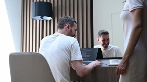 Young man working remotely on a laptop receives support from his caring wife who Stock Footage 323879532