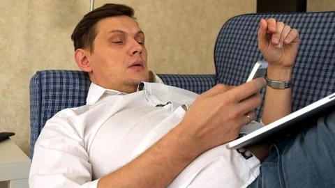 Young man working remotely lying on sofa with laptop and phone Stock Footage 86080425