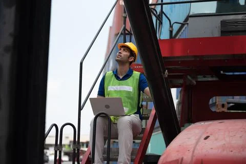 Young man working sitting on crane truck with computer at logistic import and Stock Photos
