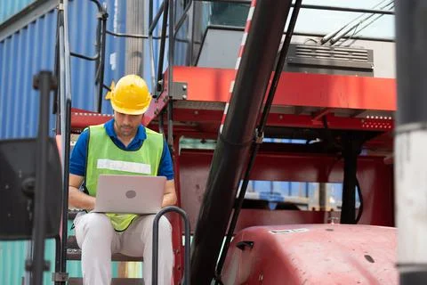 Young man working sitting on crane truck with computer at logistic import and Stock Photos
