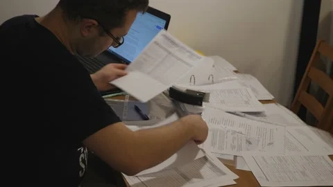 Young man working studying at night at his desk, stack of papers Stock Footage 149317957