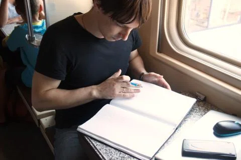 Young man working on the train, preparing to write in a large notebook with copy Stock Photos