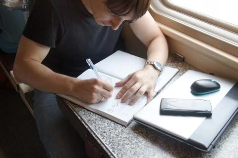 Young man working on the train, write in a large notebook with copy space Stock Photos