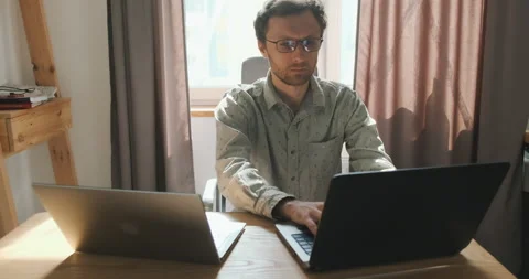 Young man is working on two laptops. Communicates by video call. Front view Stock Footage 201879261