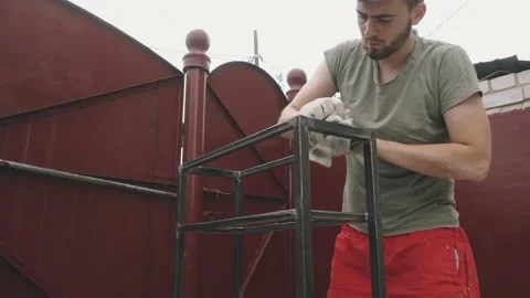 A young man in a working uniform and gloves thoroughly wipes a metal frame Vidéo 145395226