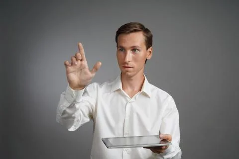 Young man working with virtual screen on grey background, holding a tablet Stock Photos