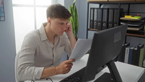 Young man at workplace in office reading documents intently on computer scr.. Stock Footage 292934279