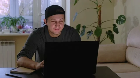 A young man works and communicates on a laptop while sitting at home. Freelancer Stock Footage 167095797