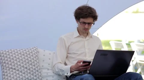 Young Man Works Behind the Notebook and Talking on the Phone Stock Footage 64126751