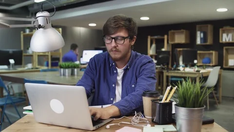 Young Man works on a computer and looks at the phone Vídeos de archivo 121773412