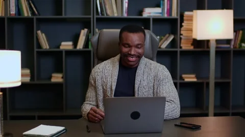 A young man works on a computer at home remotely, a man at a desk talks on a Stock Footage 263630506