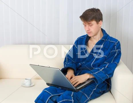 Young Man Works With Laptop In Blue Dressing Gown