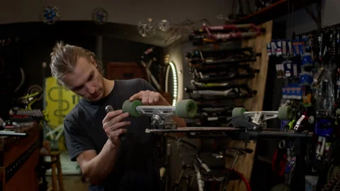 Young Man In The Workshop Attaches Wheel To Skateboard. Many Tools And Parts In 스톡 동영상 152069786