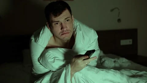 Young man wrapped in blanket sitting on bed and watching tv. Sleepy male Stock Footage 163656602