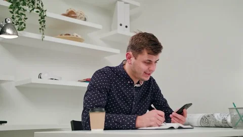 A Young Man Writing and Using a Phone Indoors. Stock Footage 83834180