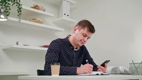 A Young Man Writing and Using a Phone Indoors. Stock Footage 83834351