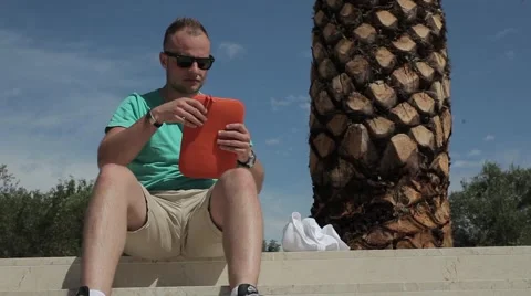 Young man writing an e-mail under the palm tree. Stock Footage 53569459