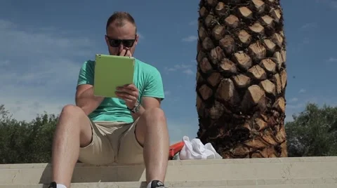 Young man writing an e-mail under the palm tree. Stock Footage 54543794