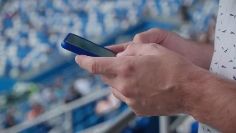A young man writing a message on his phone during a match at the stadium. Stock Footage 139932516