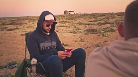Young man writing message on his phone sitting in tourist chair on sandy beach Stock Footage 192885012