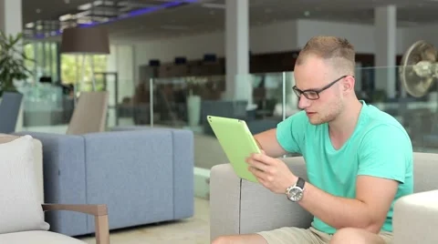 Young man writing a message on tablet from hotel lobby Stock Footage 53569428