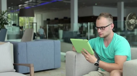 Young man writing a message on tablet from hotel lobby Stock Footage 53569434